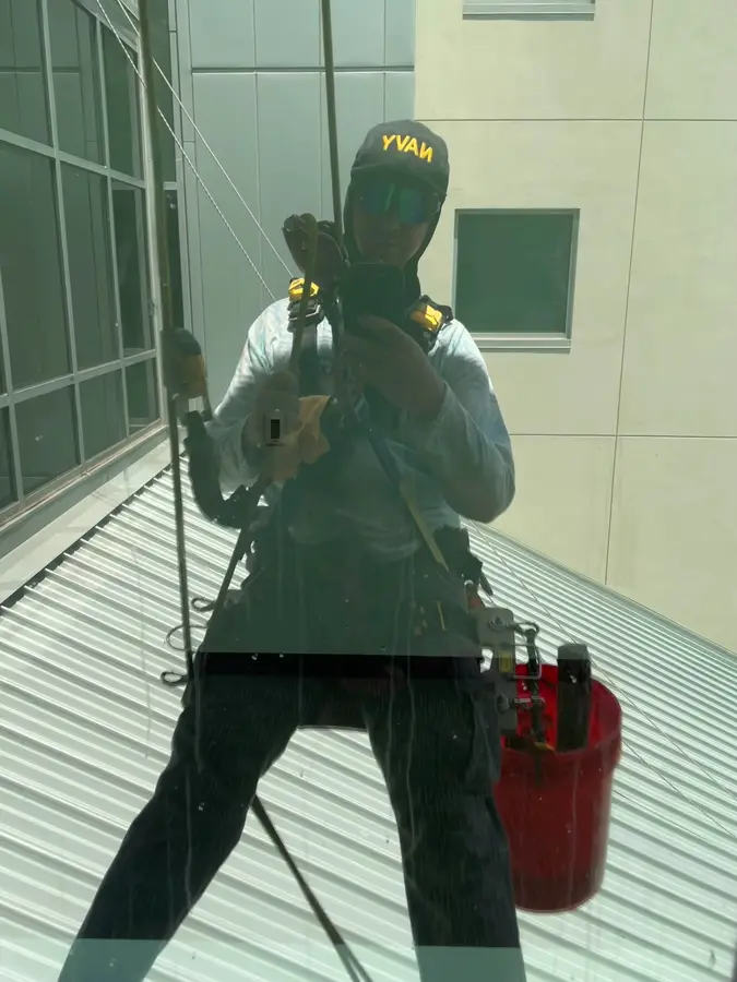 A window cleaner with squeegee and bucket, seen reflected in the glass he is cleaning