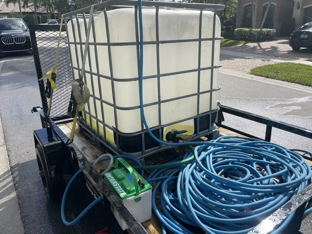The work trailer loaded with a water tank and coiled blue hoses