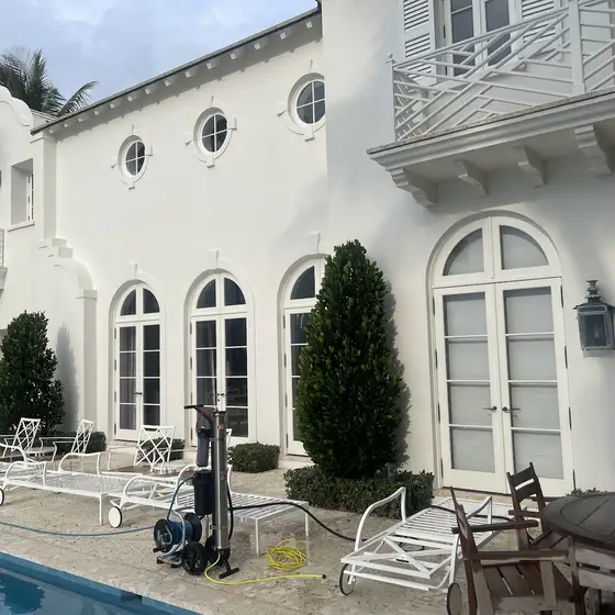 White two-storey stucco home with the pressure washer set up by the pool