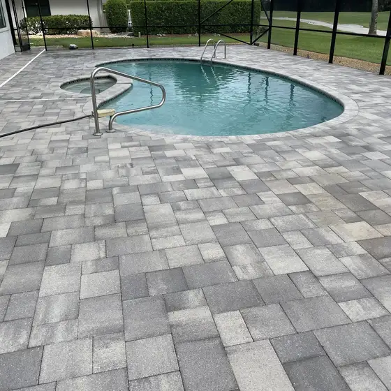 Kidney pool and grey paver deck inside a screen enclosure